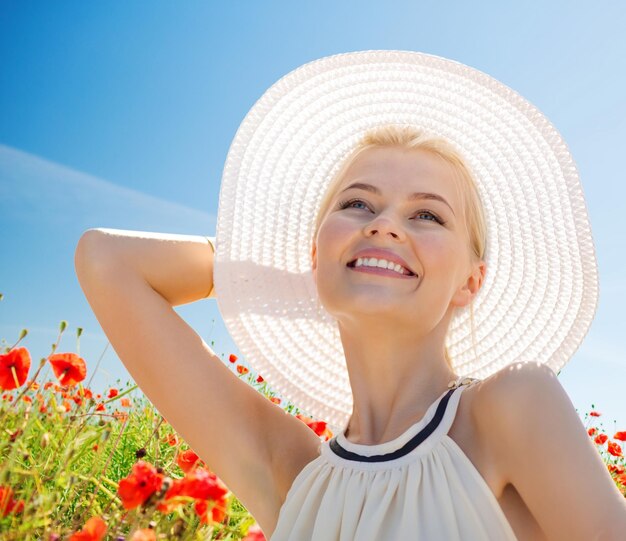 felicidad, naturaleza, verano, vacaciones y concepto de la gente - mujer joven sonriente con los ojos cerrados usando sombrero de paja en el campo de amapola