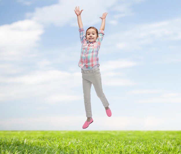 felicidad, niñez, libertad, movimiento y concepto de la gente - niñita feliz saltando en el aire sobre el cielo azul y el fondo de la hierba