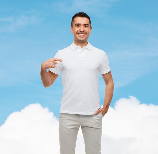 felicidad, publicidad, moda, gesto y concepto de la gente - hombre sonriente en camiseta apuntándose con el dedo sobre el cielo azul y el fondo de la nube