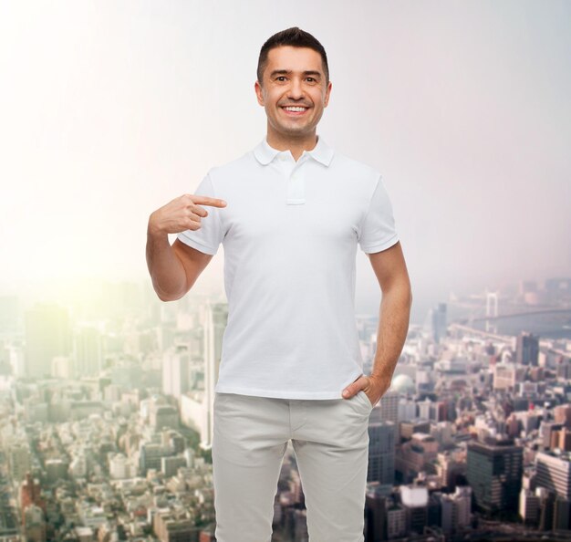 felicidad, publicidad, moda, gesto y concepto de la gente - hombre sonriente en camiseta apuntándose con el dedo sobre el fondo de la ciudad