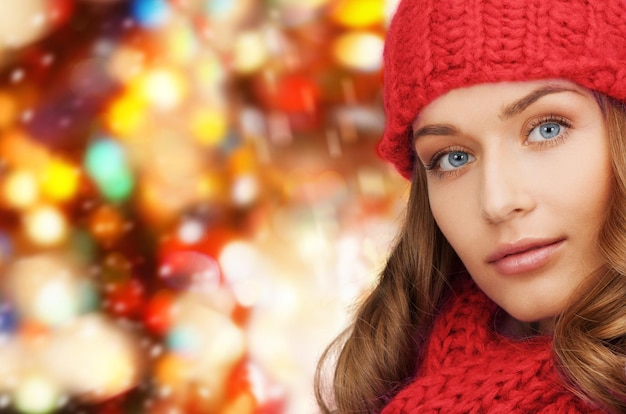 felicidad, vacaciones de invierno, navidad y concepto de la gente - cerca de una joven con sombrero y bufanda sobre fondo de luces rojas