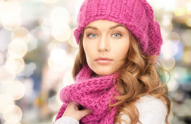 felicidad, vacaciones de invierno, navidad y concepto de la gente - cerca de una joven con sombrero rosa y bufanda sobre fondo de luces