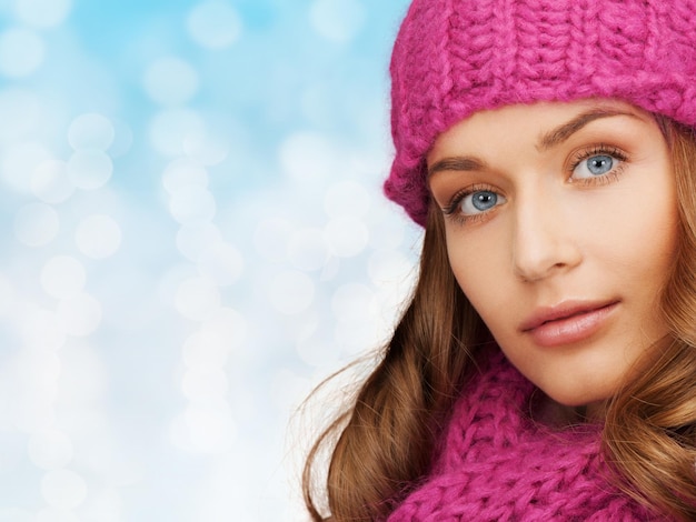 felicidad, vacaciones de invierno, navidad y concepto de la gente - cerca de una joven sonriente con sombrero rosa y bufanda sobre fondo de luces azules