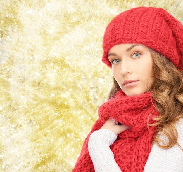 felicidad, vacaciones de invierno, navidad y concepto de la gente - mujer joven con sombrero rojo y bufanda sobre fondo de luces amarillas