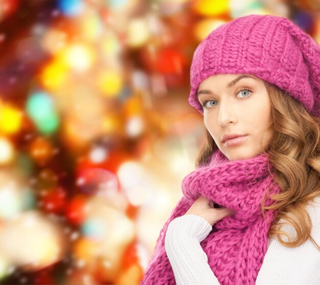 felicidad, vacaciones de invierno, navidad y concepto de la gente - mujer joven con sombrero rosa y bufanda sobre fondo de luces rojas