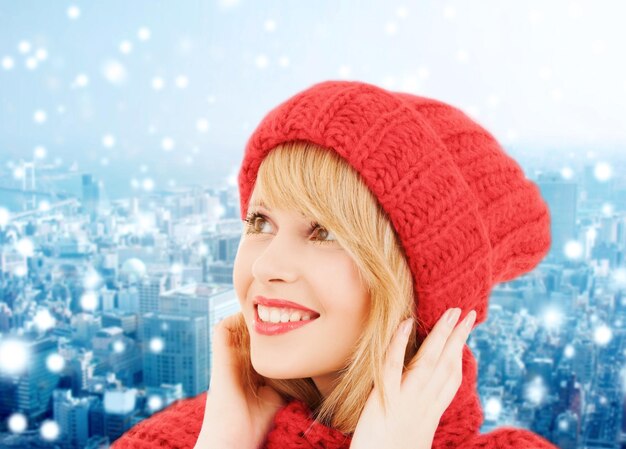 felicidad, vacaciones de invierno, navidad y concepto de la gente - mujer joven sonriente con sombrero rojo y bufanda sobre fondo azul nevado