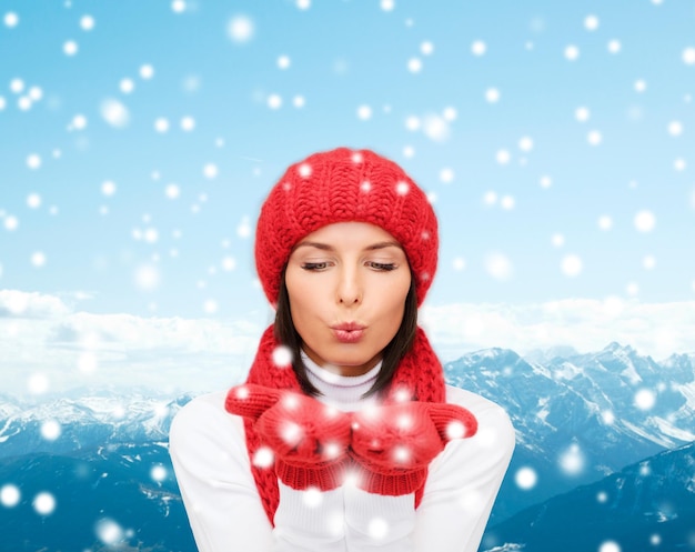 felicidad, vacaciones de invierno, turismo, viajes y concepto de personas - mujer joven sonriente con sombrero rojo y mitones sobre fondo de montañas nevadas