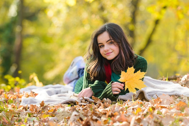 Felicidade adolescente ao ar livre no campo de outono. Menina adolescente deitada nas folhas de bordo de outono no outono ao ar livre. Belo tempo de outono na natureza.