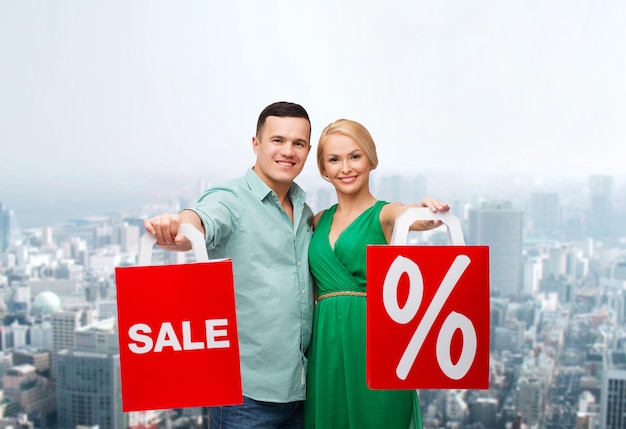 felicidade, compras e conceito de casal - casal sorridente com sacolas de compras com sinal de venda e porcentagem