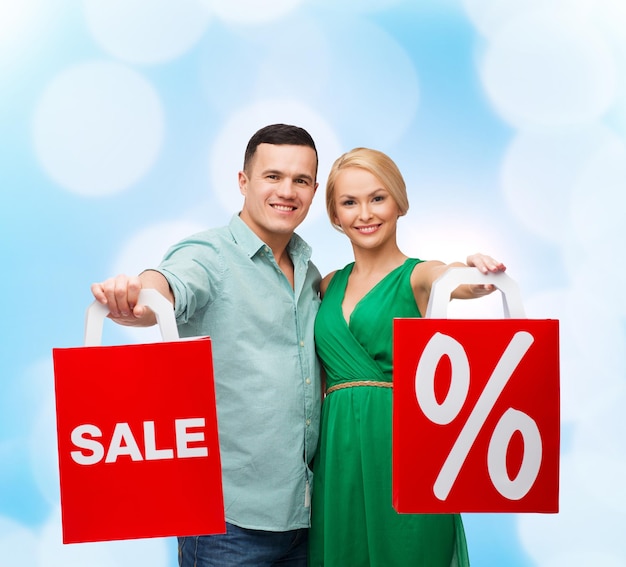 felicidade, compras e conceito de casal - casal sorridente com sacolas de compras com sinal de venda e porcentagem
