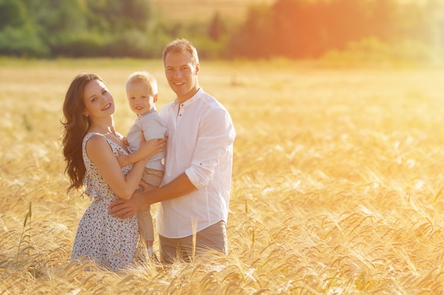Felicidade dos pais, caminhando com a criança ao ar livre. Lazer de mãe, pai e filho juntos no campo de trigo. luz solar