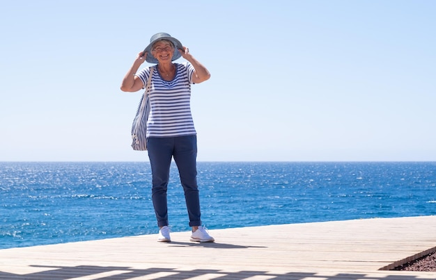 Felicidade e bom humor na mulher sorridente sênior nas férias de verão no mar Atraente senhora de cabelos brancos vestida de azul expressando liberdade e alegria Horizonte sobre a água