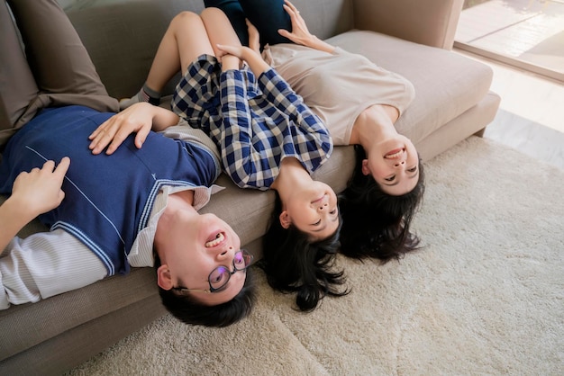 Felicidade, família asiática, mãe, pai, filha, se divertem juntos no sofá marrom com risadas e alegria
