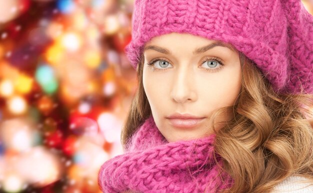 felicidade, férias de inverno, natal e conceito de pessoas - close-up de jovem de chapéu rosa e cachecol sobre fundo de luzes vermelhas
