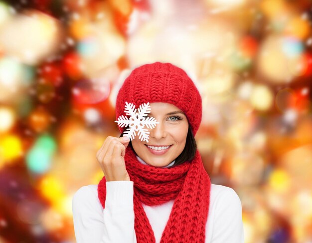 Foto felicidade, férias de inverno, natal e conceito de pessoas - jovem sorridente de chapéu vermelho, cachecol e luvas segurando fundo de luzes vermelhas de floco de neve