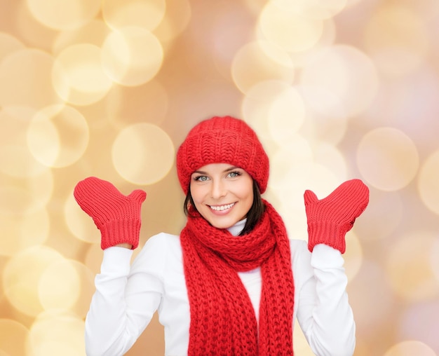 felicidade, férias de inverno, natal e conceito de pessoas - jovem sorridente de chapéu vermelho, cachecol e luvas sobre fundo de luzes bege
