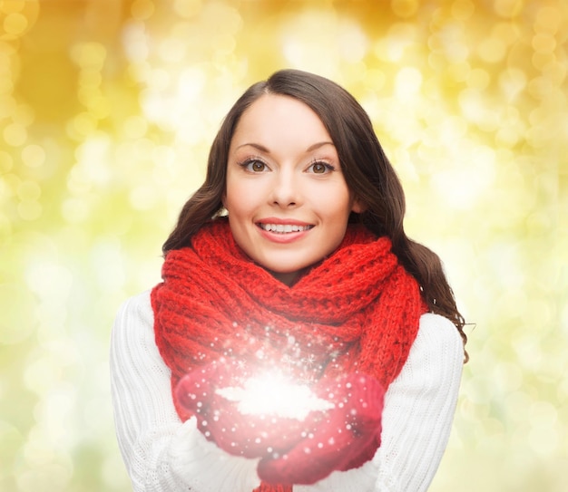 Felicidade, férias de inverno, natal e conceito de pessoas - jovem sorridente no lenço vermelho e luvas segurando floco de neve sobre fundo de luzes amarelas