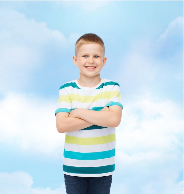 felicidade, infância e conceito de pessoas - menino sorridente em roupas casuais com braços cruzados sobre fundo de céu nublado