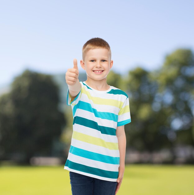 felicidade, infância, natureza e conceito de pessoas - menino sorridente em roupas casuais, mostrando os polegares sobre o fundo do parque verde