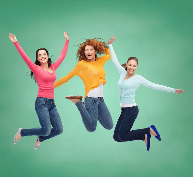 felicidade, liberdade, amizade, educação e conceito de pessoas - sorrindo jovens mulheres pulando no ar sobre fundo de placa verde