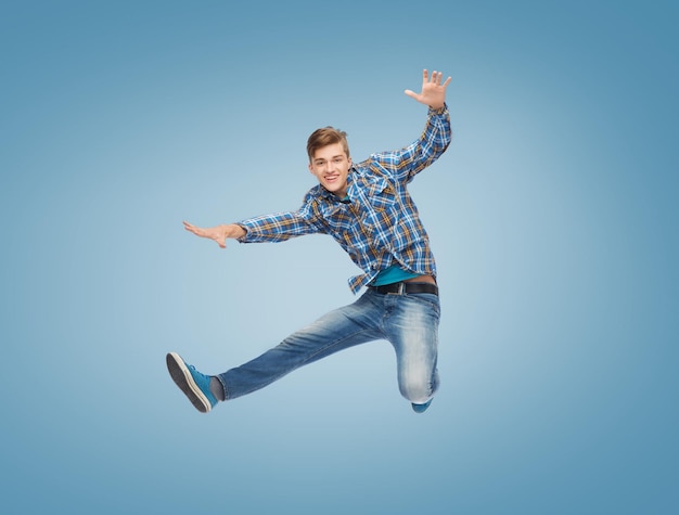 felicidade, liberdade, movimento e conceito de pessoas - jovem sorridente pulando no ar sobre fundo azul