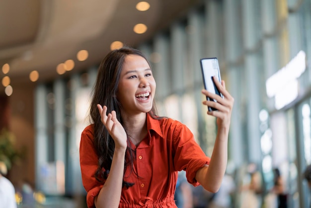 Felicidade mulher asiática sorrir onda de mão dar um beijo na família via videochamada dispositivo smartphone distanciamento social saudação com fundo desfocado shopping novo estilo de vida normal