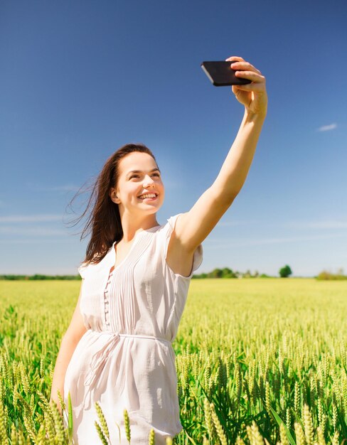 felicidade, natureza, verão, férias e conceito de pessoas - jovem sorridente com smartphone no campo de cereais