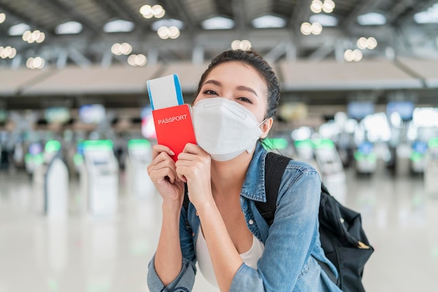 Felicidade sorridente mulher adulta asiática usar máscara facial gesto de mão mostrando passaporte e smartphone de tela em branco no aeroporto terminalasian feminino pronto para viajar após o bloqueio ia no aeroporto