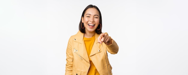 Felicidades eres tú Feliz hermosa mujer asiática riéndose señalando con el dedo a la cámara eligiendo invitar a la gente a reclutar de pie sobre fondo blanco