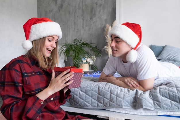 Felicitaciones de Navidad a casa. Feliz pareja sonriente con caja de regalo con gorro de Papá Noel