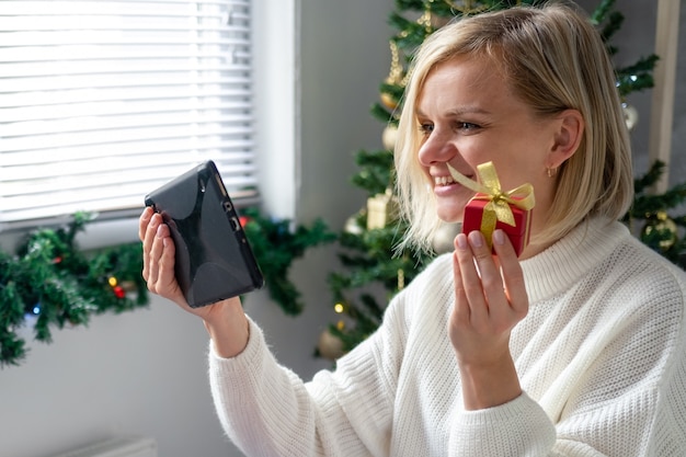 Felicitaciones de Navidad en línea. Mujer sonriente con tableta móvil para videollamadas a amigos y padres