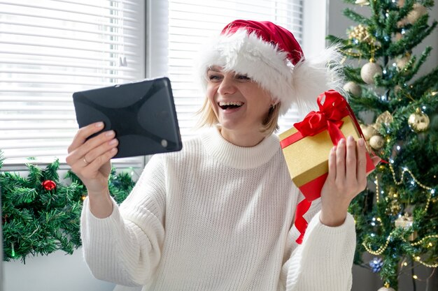 Felicitaciones de Navidad en línea. Mujer sonriente con tableta móvil para videollamadas a amigos y padres