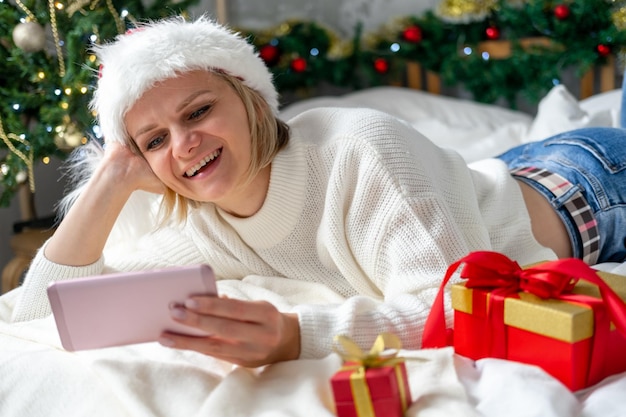 Felicitaciones navideñas en línea Mujer sonriente que usa el teléfono móvil para hacer videollamadas a amigos y padres