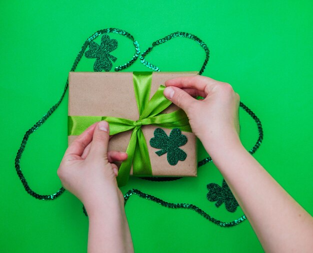 Feliz 17 de marzo. Día de San Patricio. El símbolo del festival irlandés. Vista superior desde arriba, una caja de regalo con una cinta de raso verde envuelta en papel kraft, hojas de trébol sobre un fondo verde.