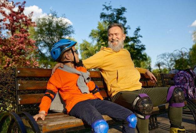 Feliz abuelo y nieto descansan en un banco después de correr en patines