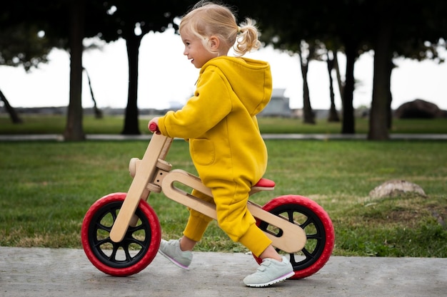 Feliz activa bastante linda caucásica rubia niña niño niño pequeño sonriente de unos 2 años de edad usando puentes amarillos brillantes aprendiendo a montar bicicleta de equilibrio en el parque de verano al aire libre