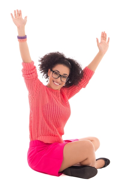 Feliz adolescente afro-americana em rosa sentado isolado no fundo branco