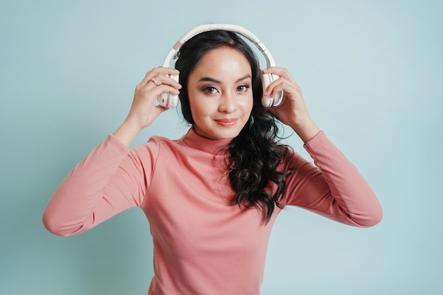 Foto feliz adolescente asiática escuchar música en auriculares sobre fondo azul claro