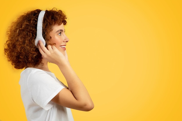 Feliz adolescente caucásica chica rizada con auriculares inalámbricos escuchando música disfrutando del tiempo libre