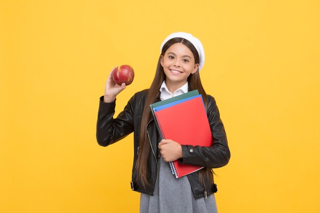 Feliz adolescente em idade escolar segura livros e saboroso café da manhã escolar com fundo amarelo maçã