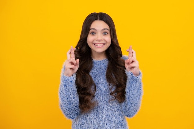 Feliz adolescente emoções positivas e sorridentes de adolescente Criança adolescente segurando os dedos cruzados para dar sorte A menina reza e espera que os sonhos se tornem realidade isolados no fundo amarelo