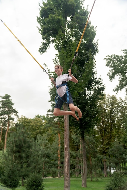 Feliz adolescente rindo pendurado em estilingues pula alto no trampolim em um parque de diversões Adolescente está se divertindo