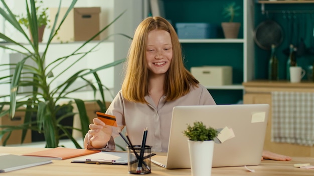 Foto feliz adolescente ruiva fazendo compras on-line com um cartão do consumidor doméstico