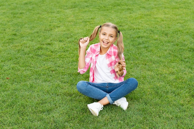 Feliz adolescente sentado na grama verde ao ar livre