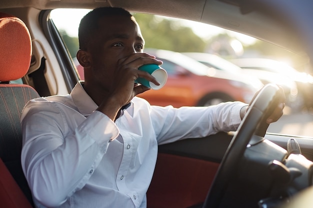 Feliz afroamericano conduciendo un coche con café, en el verano