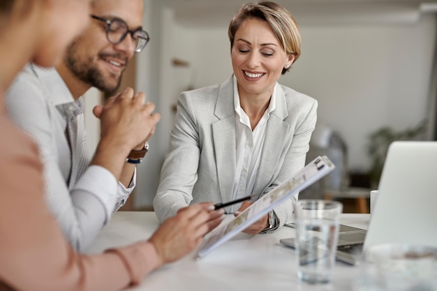 Feliz agente inmobiliario analizando planes de vivienda con una pareja durante una reunión en la oficina