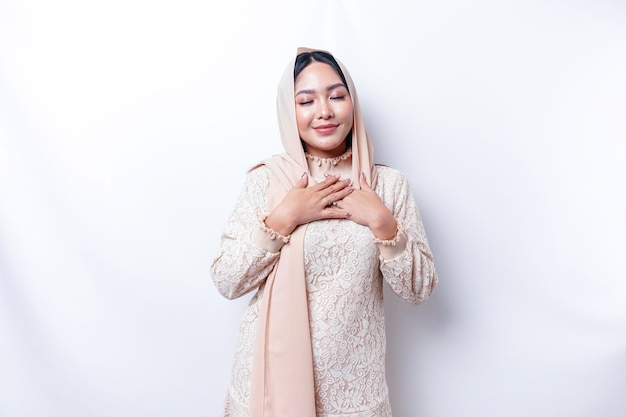 Feliz, agradecida, joven mujer asiática musulmana con la mano en el pecho sonriendo aislada de fondo blanco