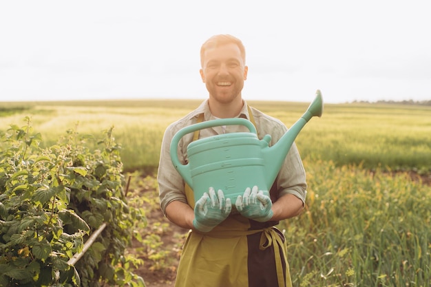 Feliz agricultor masculino segurando regador no jardim de verão