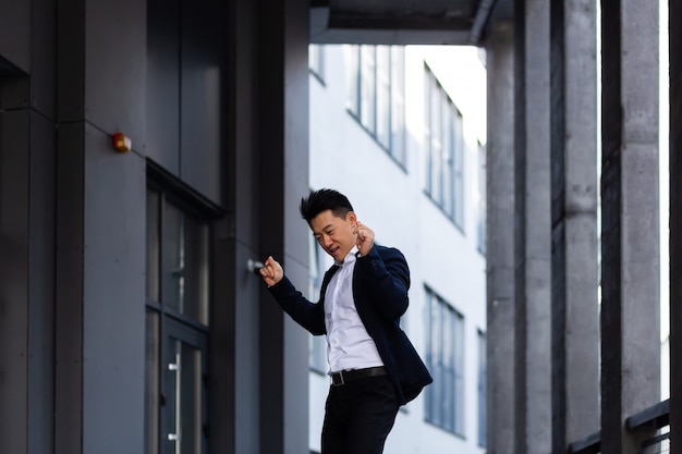 Feliz y alegre empresario asiático bailando cerca de la oficina se regocija en la victoria y el éxito