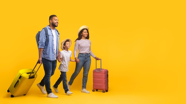 Feliz y alegre familia afroamericana de tres personas caminando con maletas